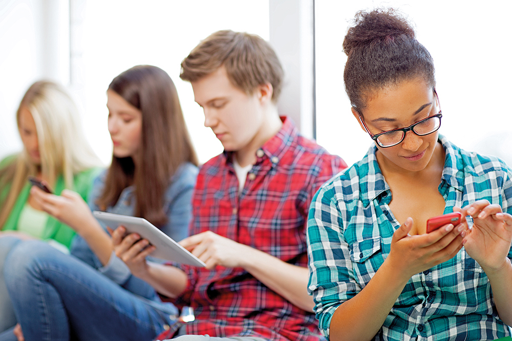technology and internet concept - students looking into phones and tablet pc at school