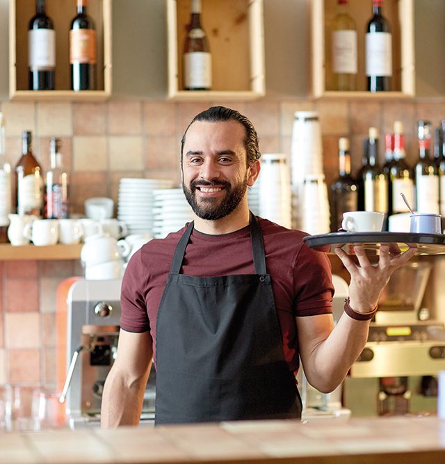 small business, people and service concept - happy man or waiter in apron holding tray with coffee cup and sugar-bowl at bar