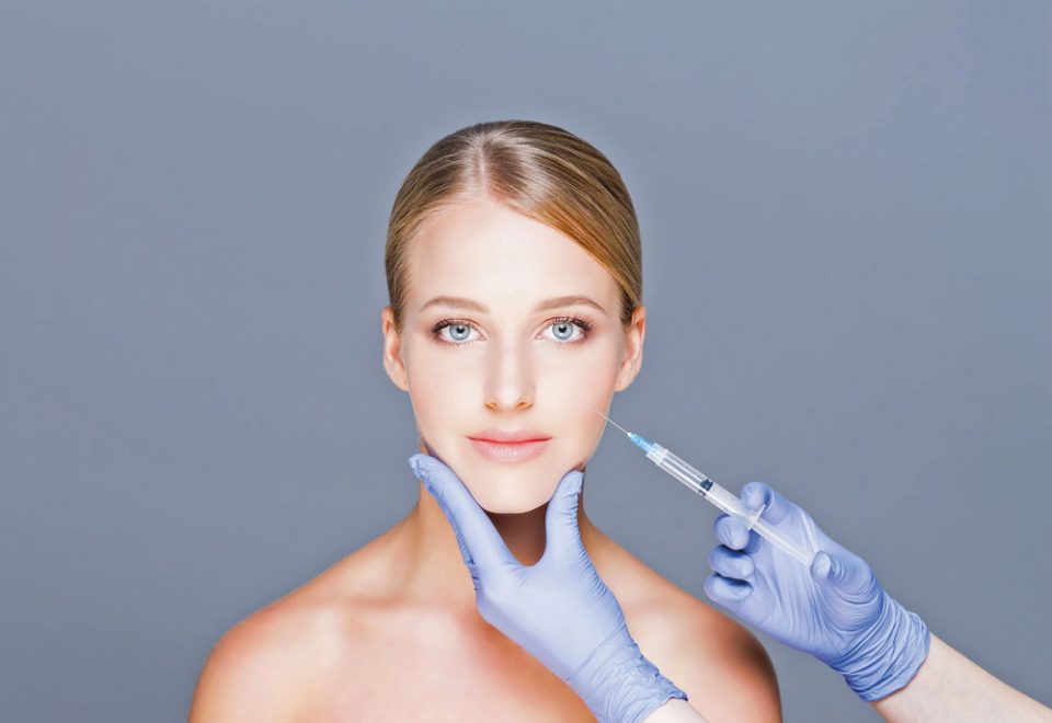 Doctor injecting botox in a beautiful face of a young woman. Plastic surgery concept.